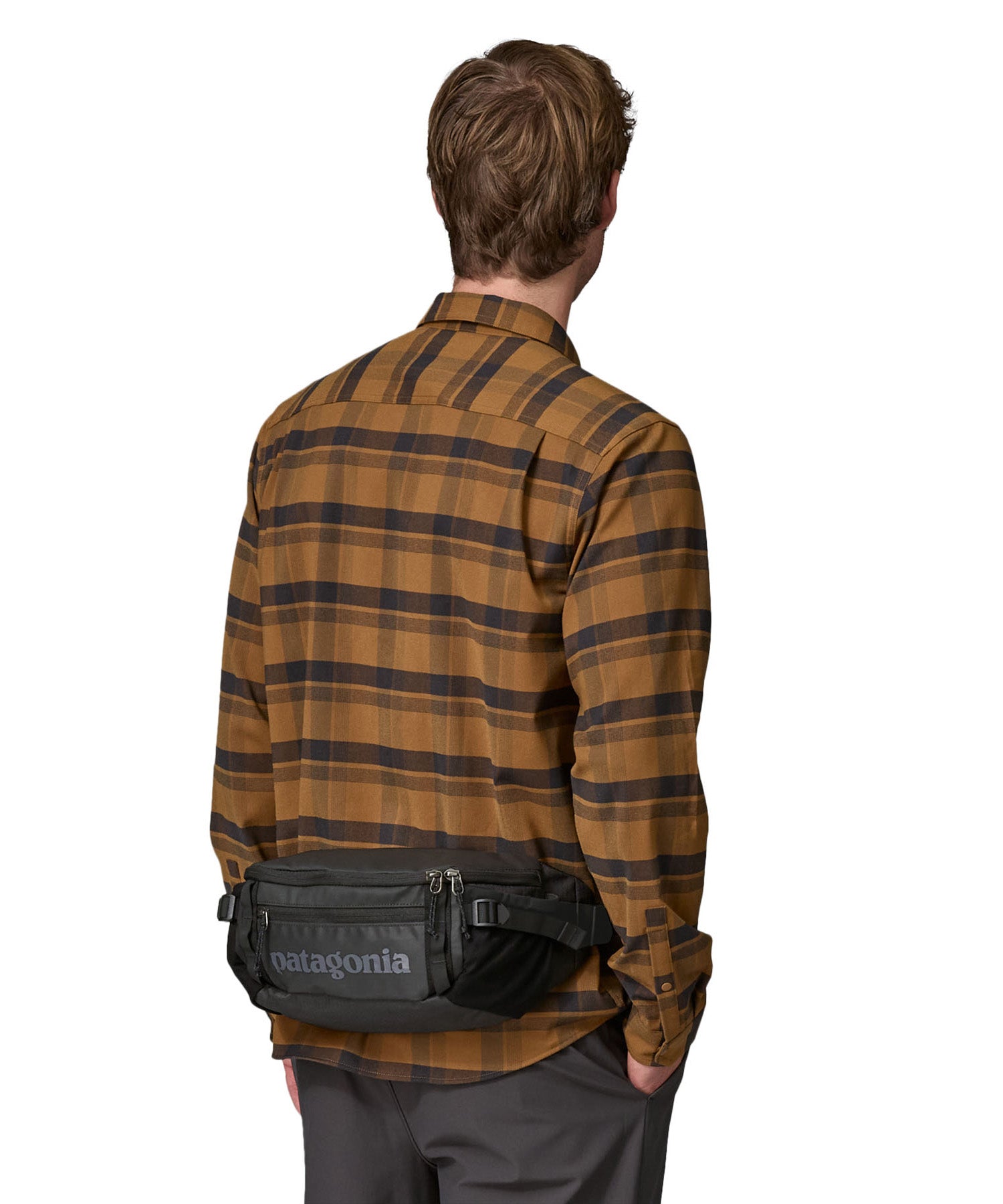 A man facing forwarding and wearing  the Patagonia waist pack in black around the waist . A 100% recycled material pack with 2 main compartments, side mesh pockets and a adjustable strap 