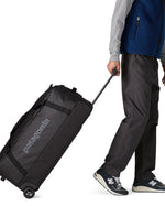 Person pulling along the Patagonia black hole wheeled 100L duffel bag in black by the pull up handle.
