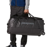 Person carrying the Patagonia black hole wheeled 100L duffel bag in black by the carry handles.