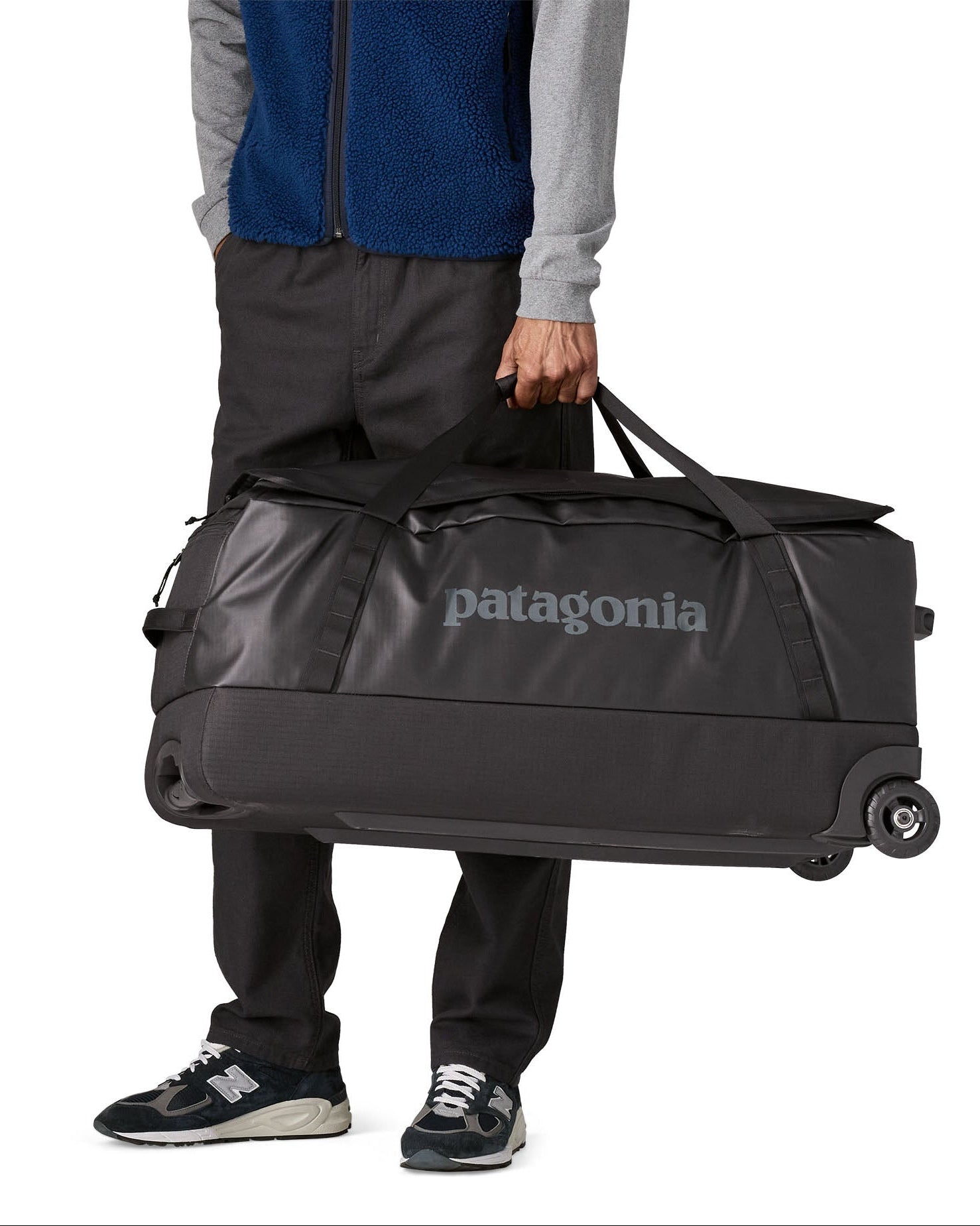 Person carrying the Patagonia black hole wheeled 100L duffel bag in black by the carry handles.