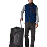 Person holding the pull handle on the Patagonia black hole wheeled 100L duffel bag in black.