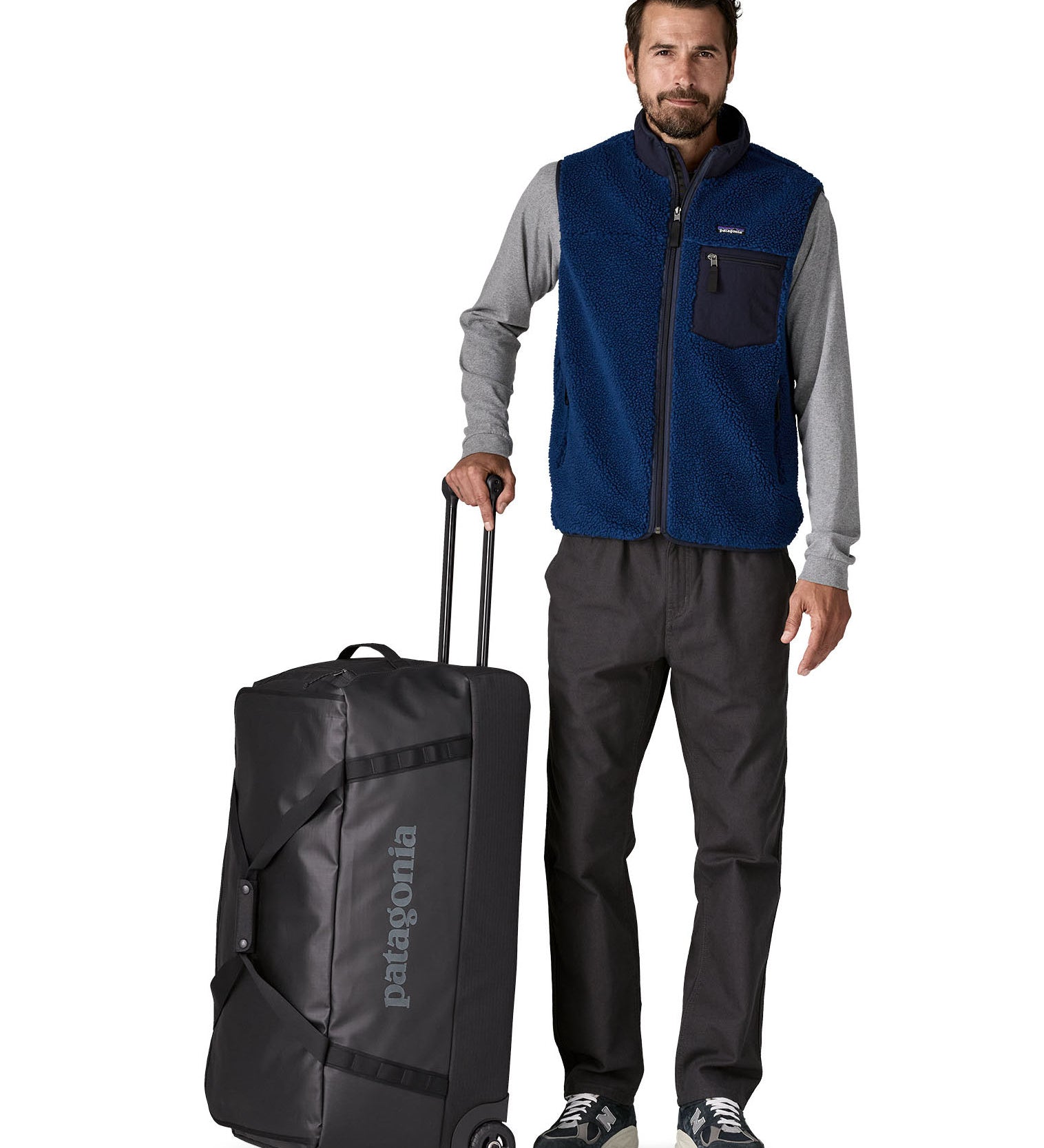 Person holding the pull handle on the Patagonia black hole wheeled 100L duffel bag in black.