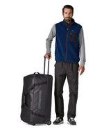 Person holding the pull handle on the Patagonia black hole wheeled 100L duffel bag in black.