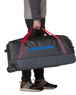 Patagonia black hole wheeled large capacity 100L duffel bag in black with red strap carry handles and blue logo on front.