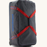 Patagonia black hole wheeled large capacity 100L duffel bag in black with red strap and blue logo on front.