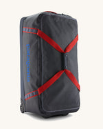 Patagonia black hole wheeled large capacity 100L duffel bag in black with red strap and blue logo on front.