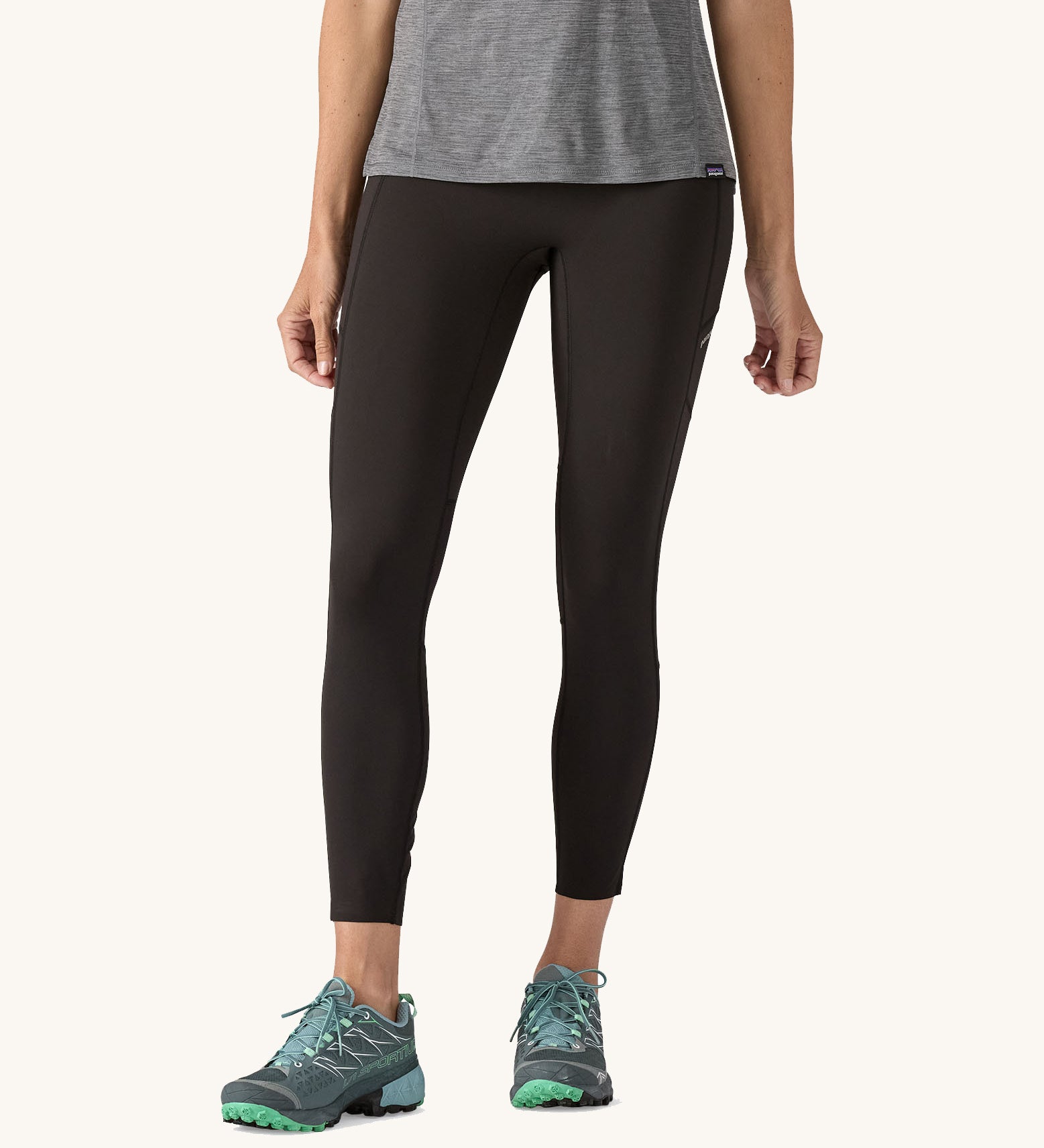 A woman wearing a pair of black Patagonia running 7/8 tights on a cream background.