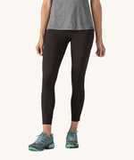 A woman wearing a pair of black Patagonia running 7/8 tights on a cream background.