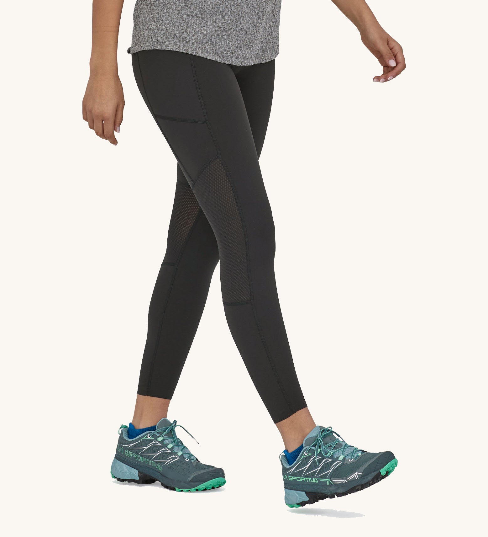 A woman walking in the black Patagonia running 7/8 tights on a cream background.