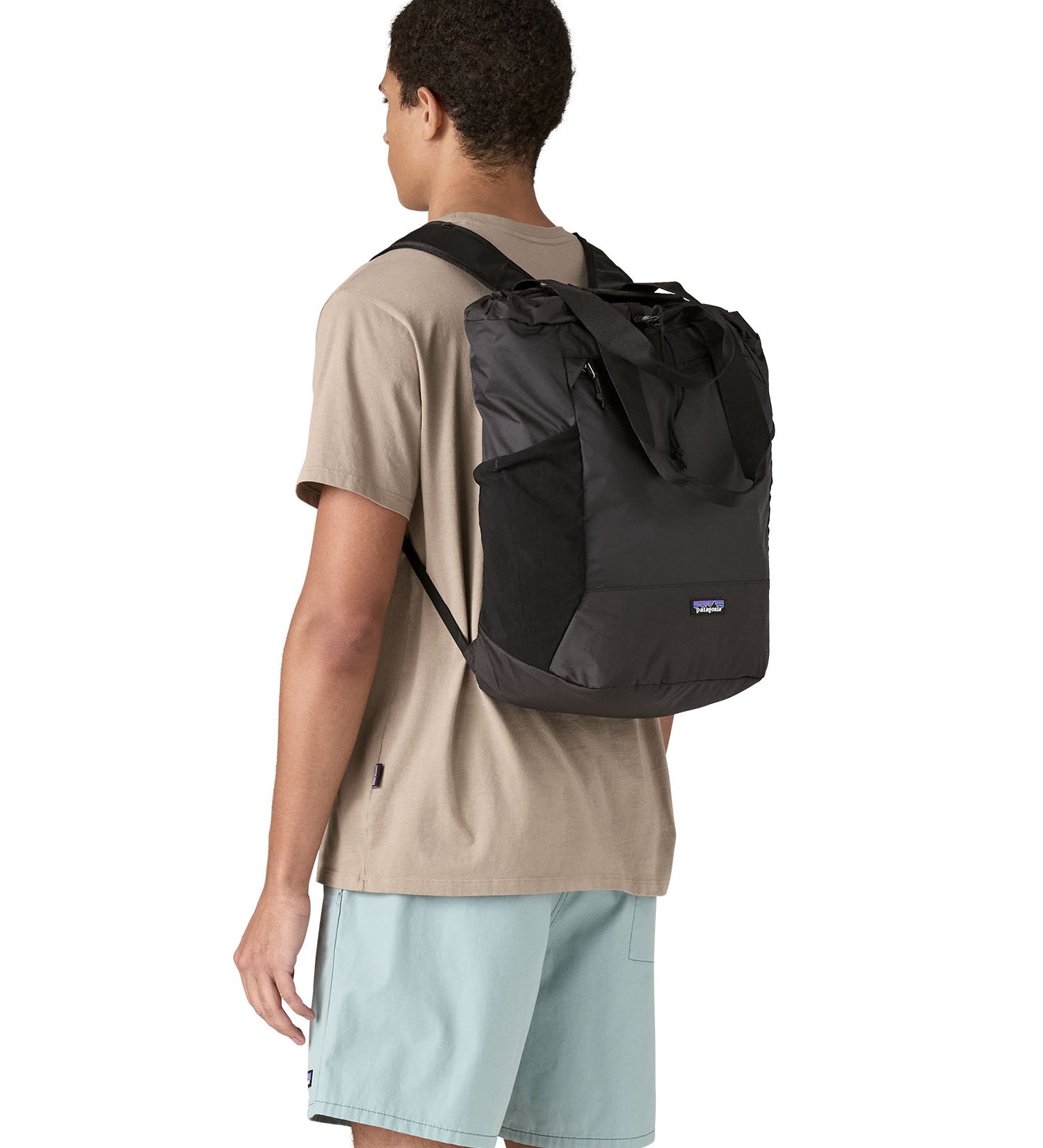 Patagonia Terravia tote bag in black worn by a adult on the back showing the carrying handle details and side pockets for holding bottles