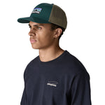 A man wearing the Patagonia adult cascade green hat. A trucker style cap with a mesh back and logo embroidery on the front panel available at Babipur.
