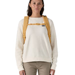 Patagonia yellow 26L day refugio backpack with a buttercup design worn by an adult shoulder straps and clip detail