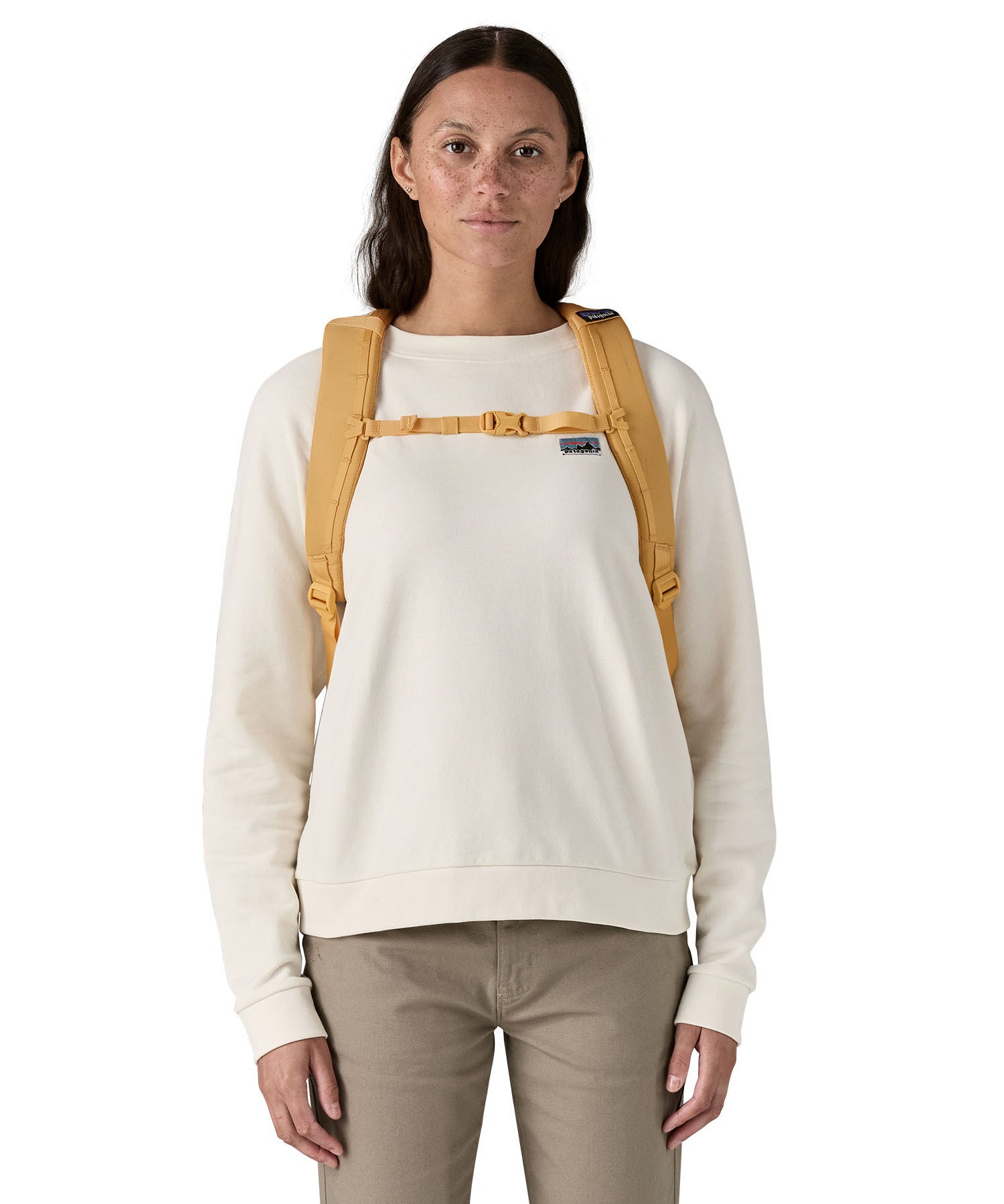 Patagonia yellow 26L day refugio backpack with a buttercup design worn by an adult shoulder straps and clip detail