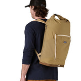 Person wearing the Patagonia fieldsmith roll top backpack in classic tan with zipped compartments and small blag logo tag on front.