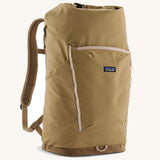 Patagonia fieldsmith roll top backpack in classic tan with zipped compartments and small blag logo tag on front.
