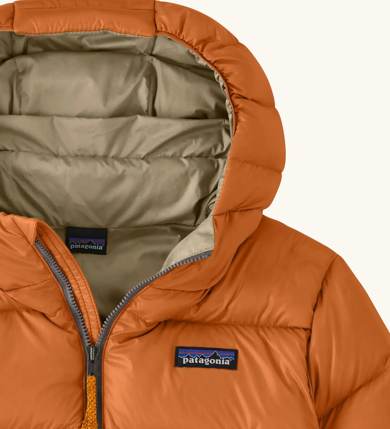 Close up of the muted yellow lined hood on the Patagonia kids hi-loft down sweater hoody windproof jacket in marigold orange.