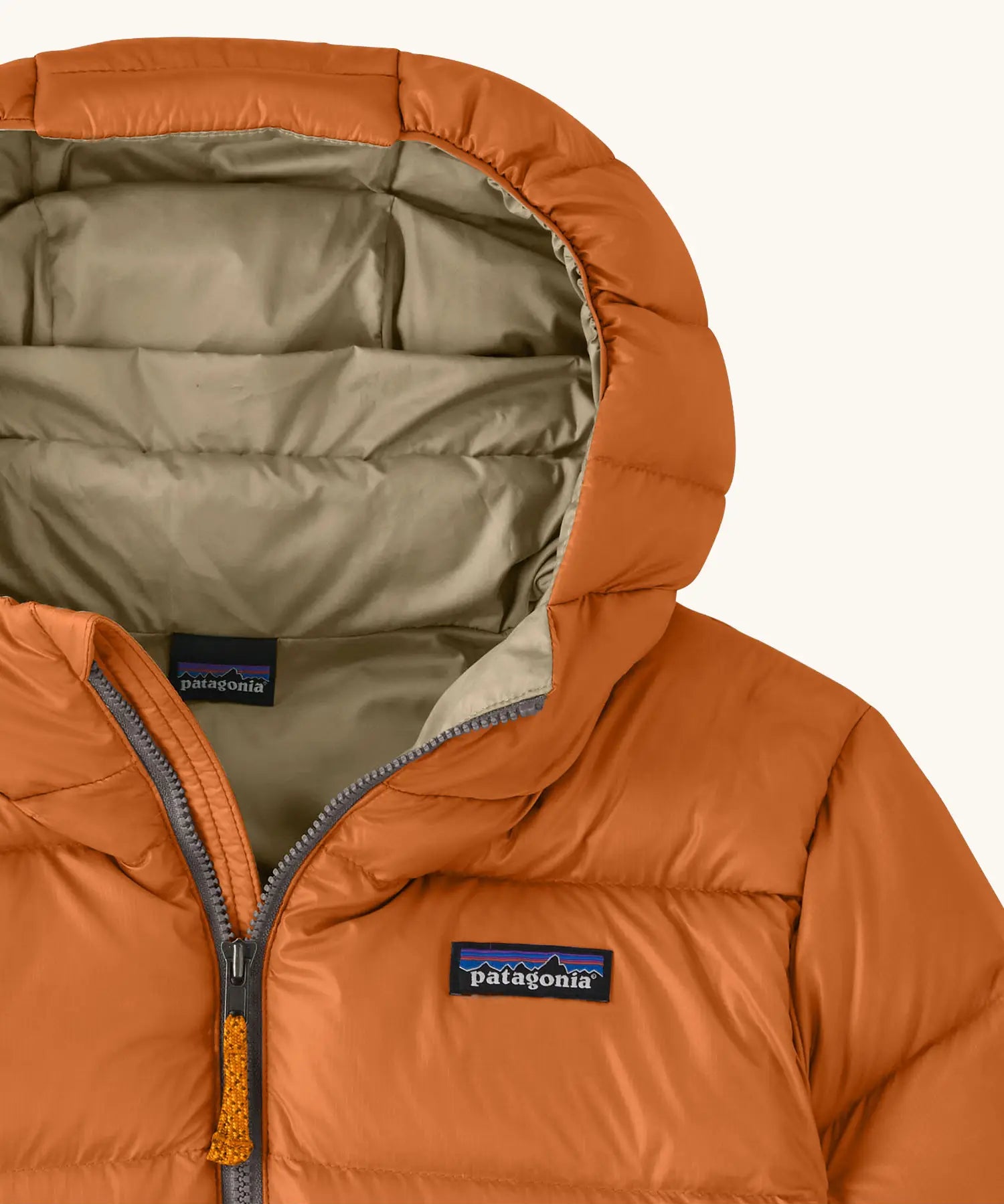 Close up of the muted yellow lined hood on the Patagonia kids hi-loft down sweater hoody windproof jacket in marigold orange.