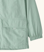 Close up of Patagonia kid's outdoor everyday hooded jacket in light green  showing front velcro pocket and elasticated cuff 