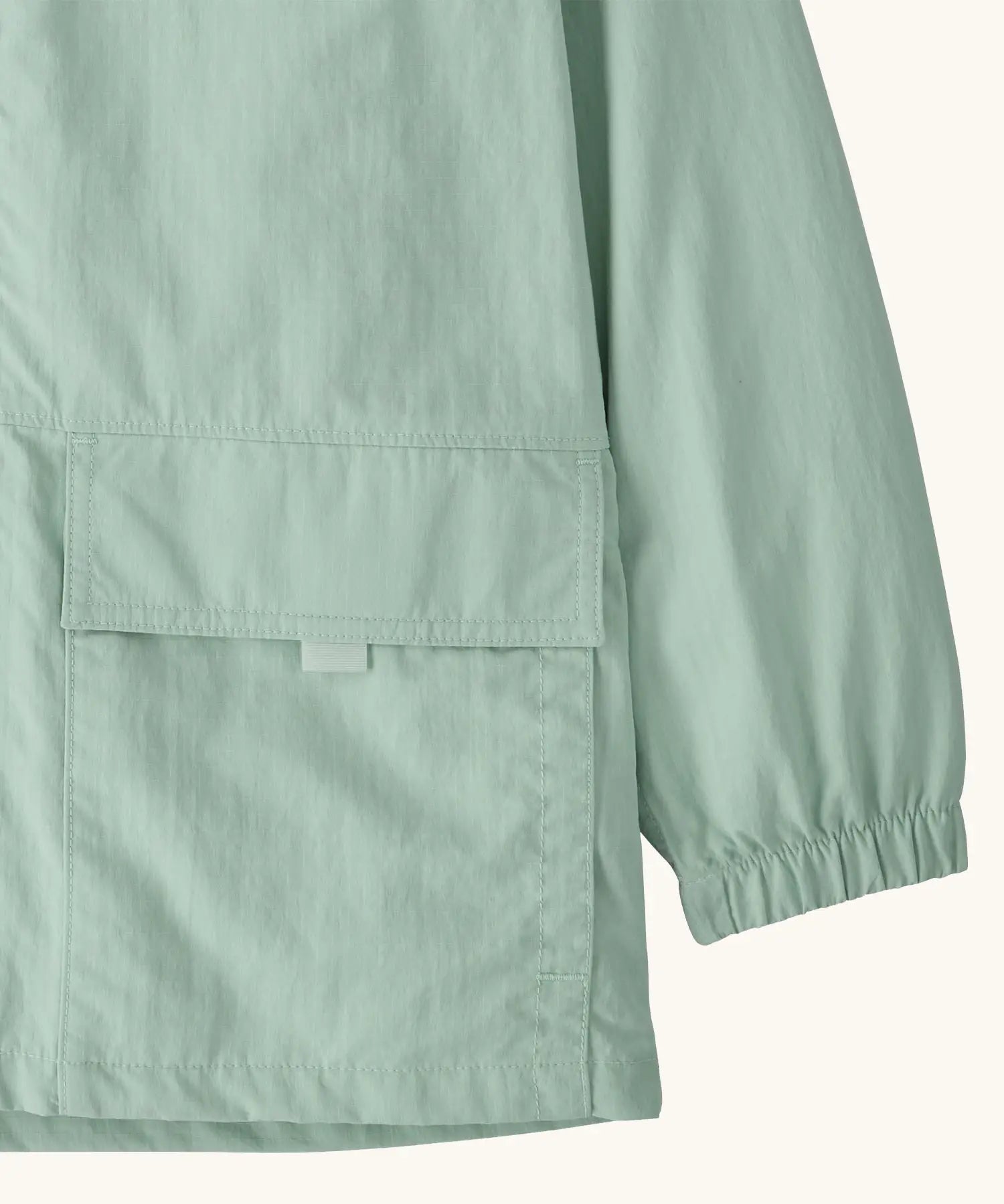 Close up of Patagonia kid's outdoor everyday hooded jacket in light green  showing front velcro pocket and elasticated cuff 