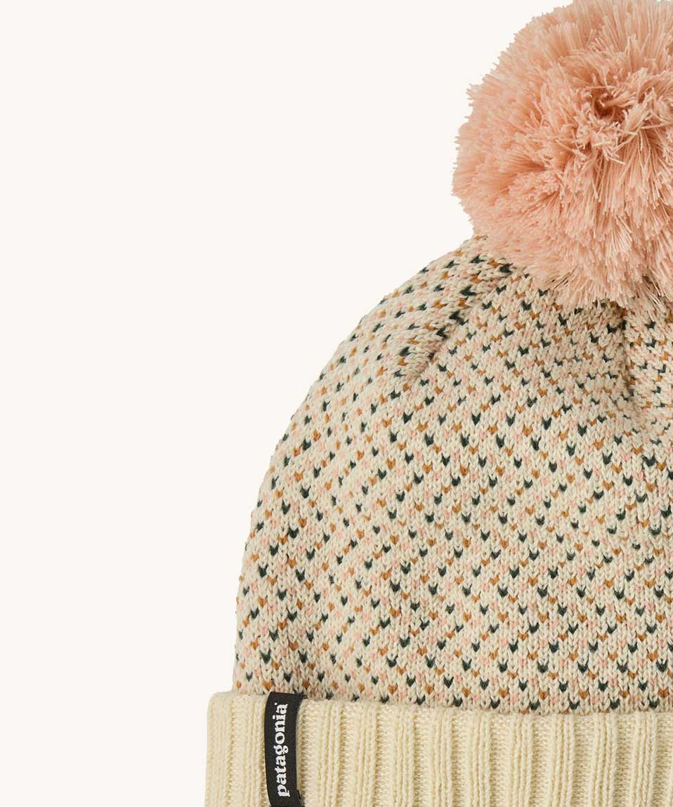 A close up of the Patagonia kids powder town beanie in confetti/natural. A thick beanie with blue and yellow speckled on natural coloured organic fabric. Features a light pink pom pom on top.