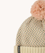 A close up of the Patagonia kids powder town beanie in confetti/natural. A thick beanie with blue and yellow speckled on natural coloured organic fabric. Features a light pink pom pom on top.