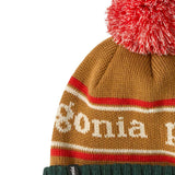 A close up of the Patagonia Kids  Powder Town Beanie in park stripe talon gold colour. A gold beanie with a green turn up brim. Features a red and white pompom on top and the brand name across the middle in white
