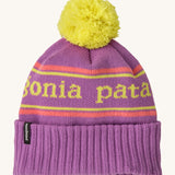 Patagonia kids powder town beanie in park stripe/brisk purple. A thick beanie with the brand name in yellow through the middle on bright purple organic fabric. Features a bright yellow pom pom on top.