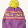 Patagonia kids powder town beanie in park stripe/brisk purple. A thick beanie with the brand name in yellow through the middle on bright purple organic fabric. Features a bright yellow pom pom on top.
