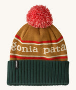 Patagonia Kids  Powder Town Beanie in park stripe talon gold colour. A gold beanie with a green turn up brim. Features a red and white pompom on top and the brand name across the middle in white