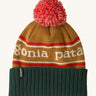 Patagonia Kids  Powder Town Beanie in park stripe talon gold colour. A gold beanie with a green turn up brim. Features a red and white pompom on top and the brand name across the middle in white