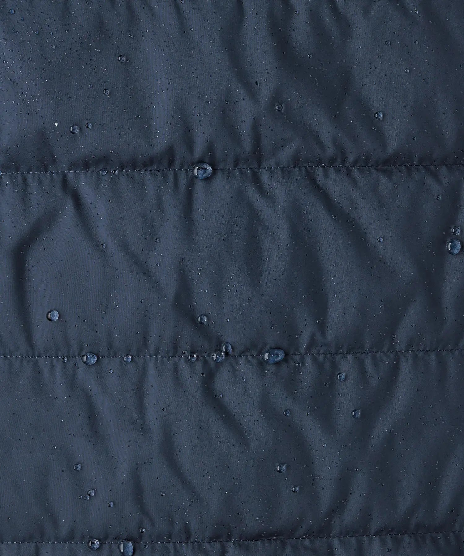 Close up of water droplets pooling on material of the patagonia kids reversible ready freddy hoody water resistant jacket in new navy.