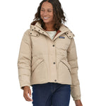 A woman with dark coloured shoulder length wavy hair wearing the Patagonia Women's Downdrift Jacket in Oar Tan