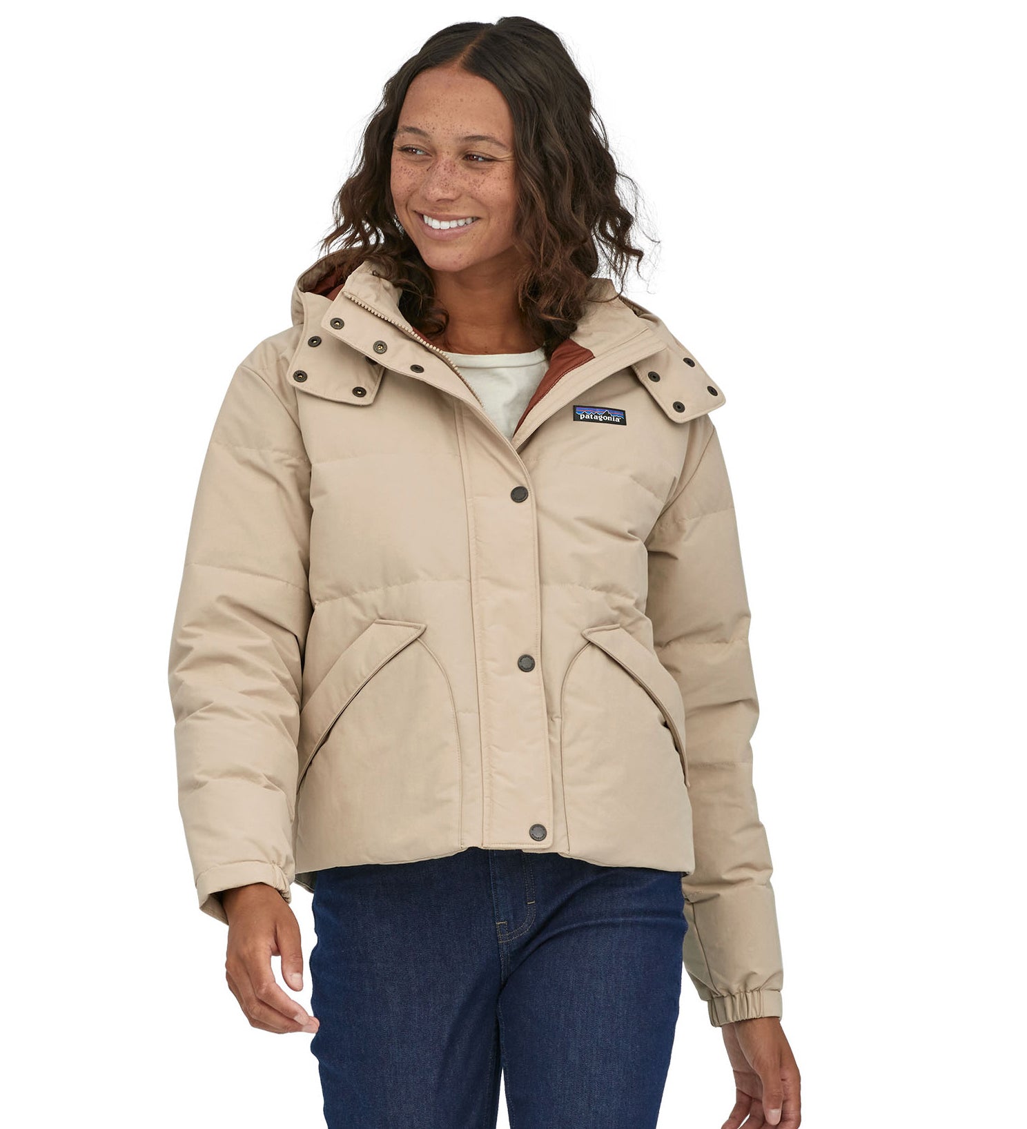 A woman with dark coloured shoulder length wavy hair wearing the Patagonia Women's Downdrift Jacket in Oar Tan