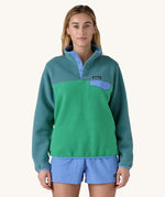 A woman wearing a Patagonia Women's Lightweight Synchilla Snap-T Fleece in a Heartleaf Green colour. 
