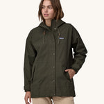 A woman wearing a Patagonia Women's Outdoor Everyday Rain Jacket in a Pine Needle Green colour. The zip of the coat is fully closed.