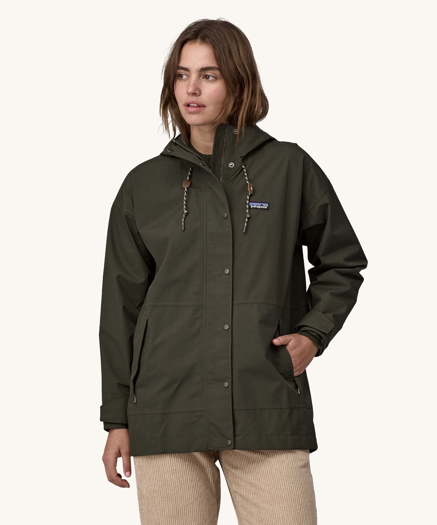 A woman wearing a Patagonia Women's Outdoor Everyday Rain Jacket in a Pine Needle Green colour. The zip of the coat is fully closed.