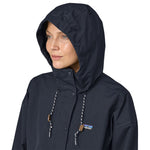 A close up of a woman with a hood up on the Patagonia Women's Outdoor Everyday Rain Jacket in a Pitch Blue colour.