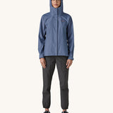A woman wearing the Patagonia Women's Torrentshell 3L Rain Jacket in a Current Blue colour with the hood up. We have a wide range of Patagonia adult's and children's coats and clothing at Babipur. 