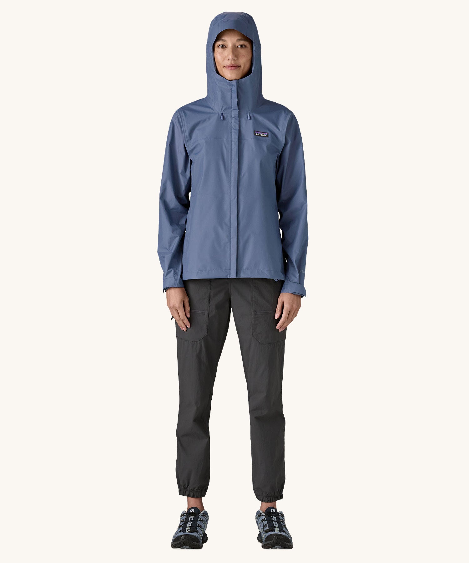 A woman wearing the Patagonia Women's Torrentshell 3L Rain Jacket in a Current Blue colour with the hood up. We have a wide range of Patagonia adult's and children's coats and clothing at Babipur. 