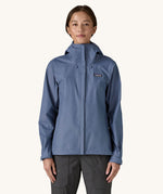 A woman wearing the Patagonia Women's Torrentshell 3L Rain Jacket in a Current Blue colour. We have a wide range of Patagonia adult's and children's coats and clothing at Babipur.