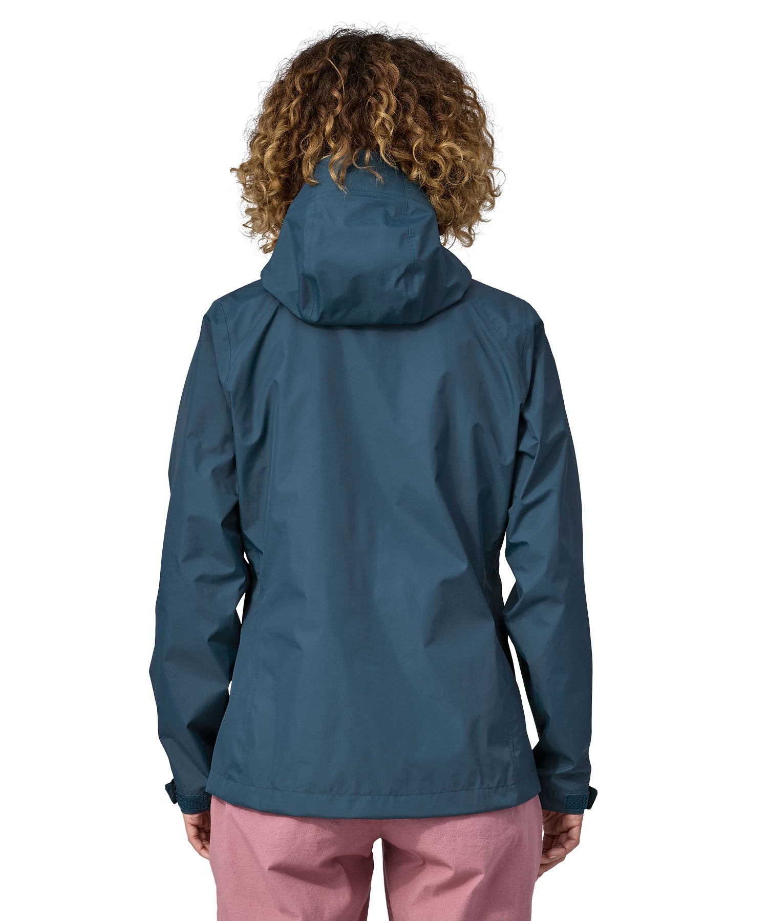 A woman wearing a Patagonia Women's Torrentshell 3L Rain Jacket in a Lagom Blue colour stood in front of a plain background. The woman is facing away showing the back of the coat. 