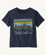 Patagonia Little Kids Fitz Roy Skies T-Shirt - New Navy. A deep, navy blue t-shirt with a fun Patagonia mountain range print in front of a striped pink, blue, purple and .yellow sky