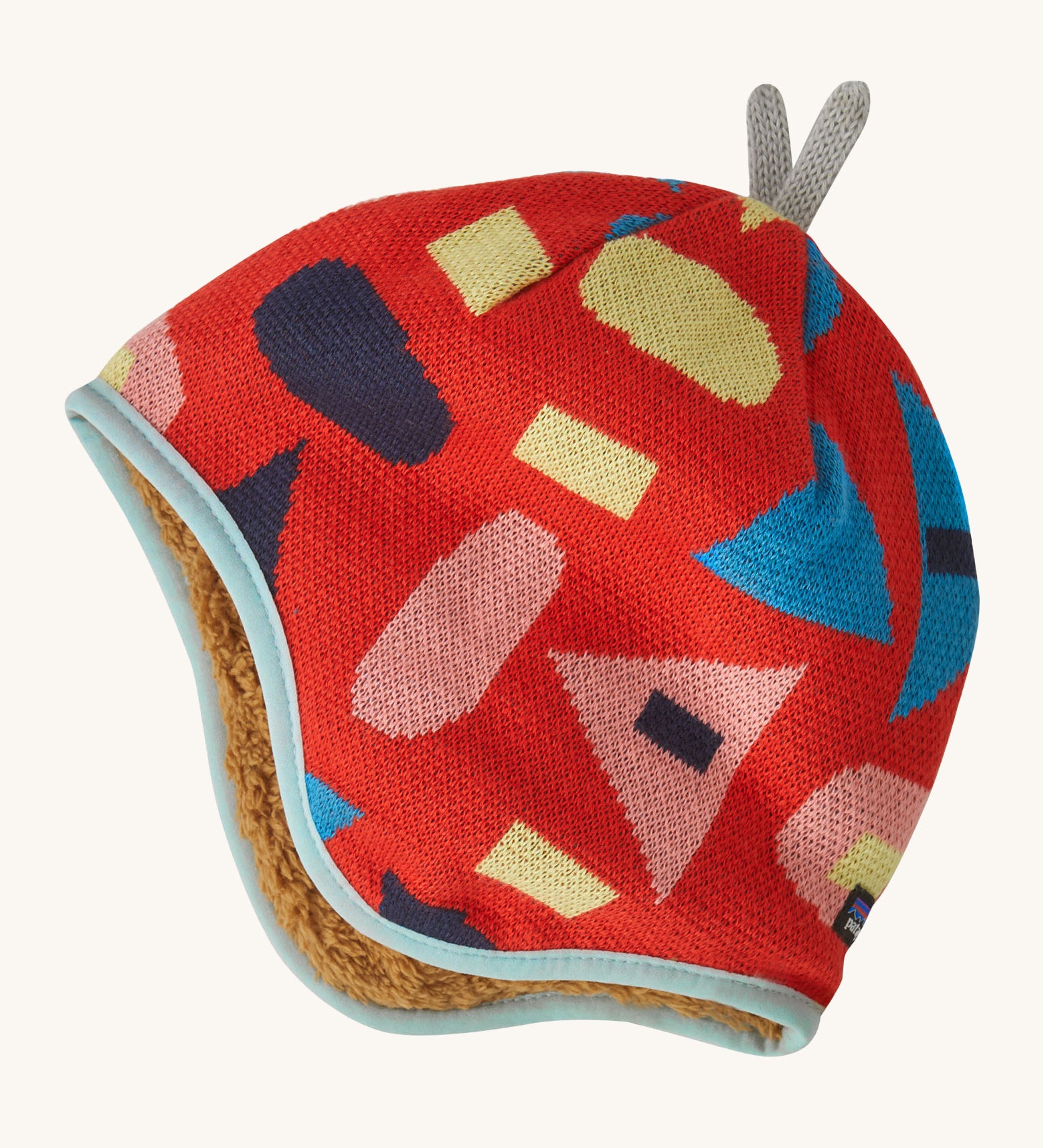 Patagonia little kids in forest being and sizzle red design. A reversible hat which features a red beanie with different coloured shapes and grey decorative tabs on top and brown fur on the inside to keep the head and ears warm. 