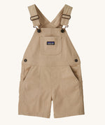 The Patagonia Little Kids Stand Up Shortalls in an Oar Tan colour on a plain background.
