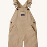 The Patagonia Little Kids Stand Up Shortalls in an Oar Tan colour on a plain background.