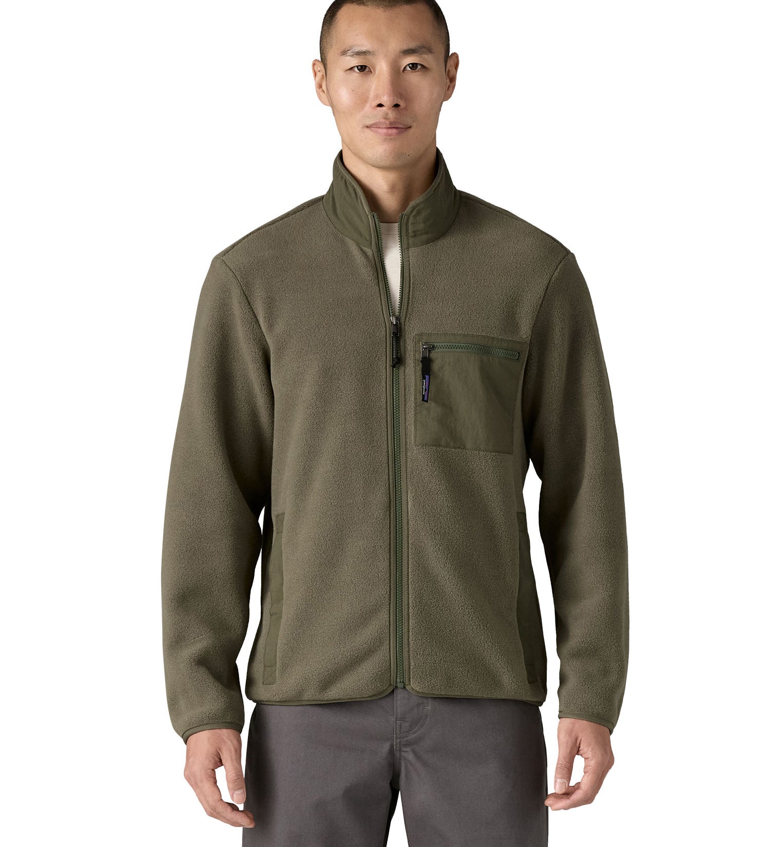 Man wearing the Patagonia Men's Synchilla® Fleece Jacket in Basin Green, a solid khaki green full zip fleece jacket. Made from Synchilla® 100% recycled fleece. Features a stand up collar handwarmer pockets and a left chest zippered patch pocket. 