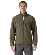 Man wearing the Patagonia Men's Synchilla® Fleece Jacket in Basin Green, a solid khaki green full zip fleece jacket. Made from Synchilla® 100% recycled fleece. Features a stand up collar handwarmer pockets and a left chest zippered patch pocket. 