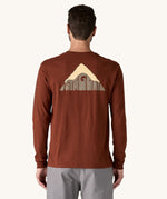 A view of the back of a man wearing a brown coloured Patagonia Men's Long Sleeved Organic T-Shirt with Driftways design. This t-shirt is a part of a wide range of Patagonia clothing and accessories available here at Babipur. 
