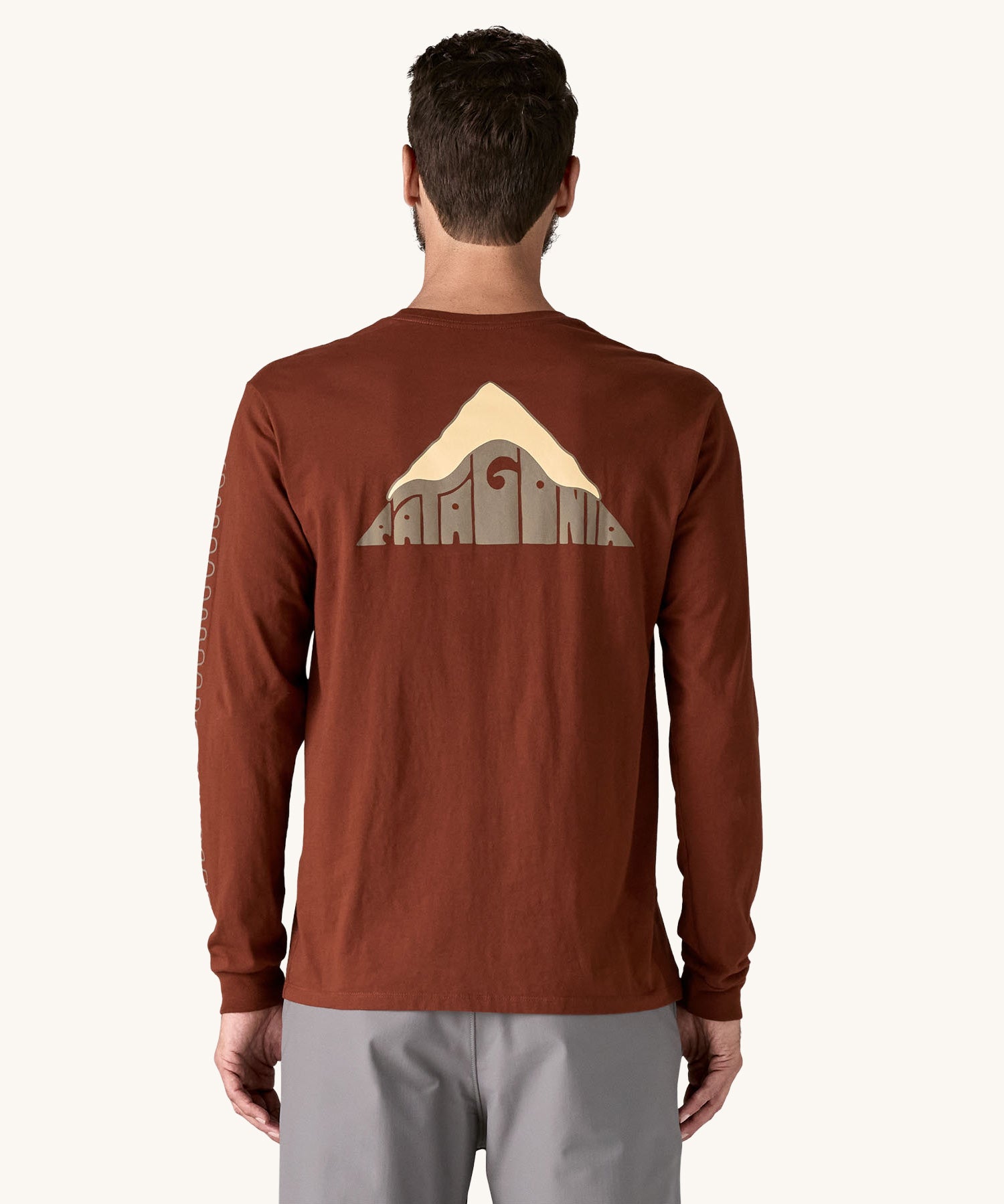 A view of the back of a man wearing a brown coloured Patagonia Men's Long Sleeved Organic T-Shirt with Driftways design. This t-shirt is a part of a wide range of Patagonia clothing and accessories available here at Babipur. 
