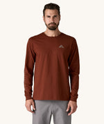 A man wearing a brown coloured Patagonia Men's Long Sleeved Organic T-Shirt with Driftways design. This t-shirt is a part of a wide range of Patagonia clothing and accessories available here at Babipur. 
